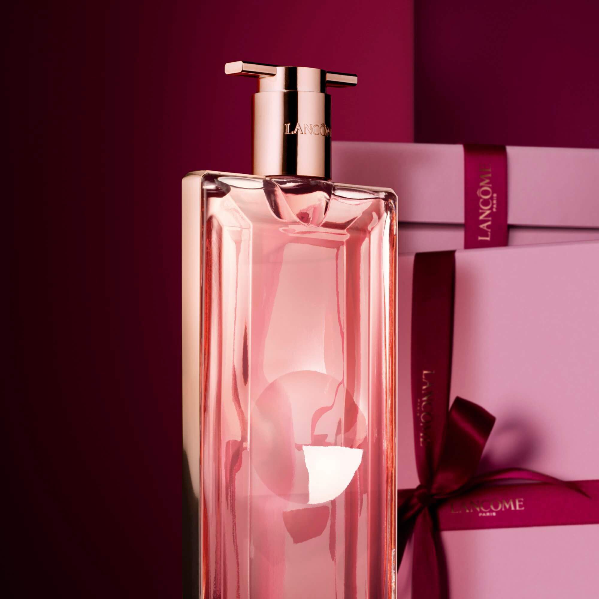 Image of Idole EDP standing in front of a pile of pink and dark red gift boxes, set against a dark red background. 