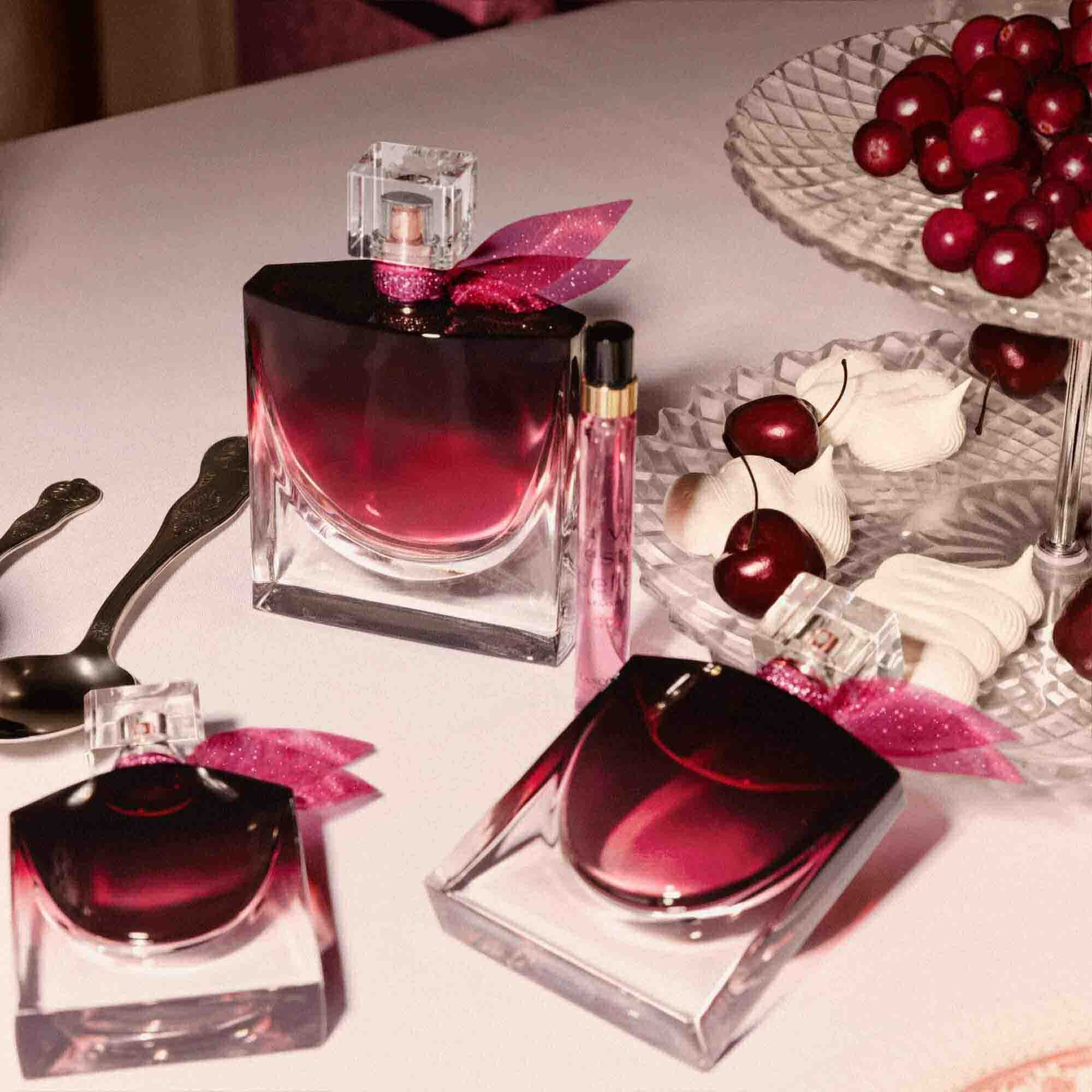An elegant tabletop scene featuring multiple sizes of the perfume bottle alongside a bowl of fresh cherries and silver spoons.	